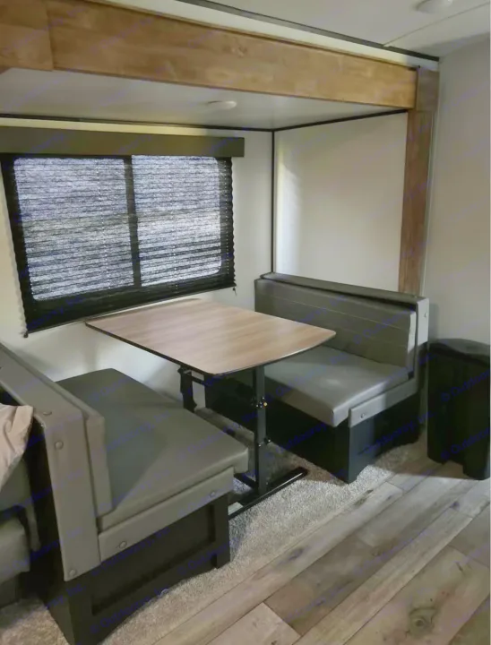 Cozy RV rental dinette: dark gray benches, light wood table, and window blinds. Perfect for meals and relaxation.. Keystone RV Springdale 2022