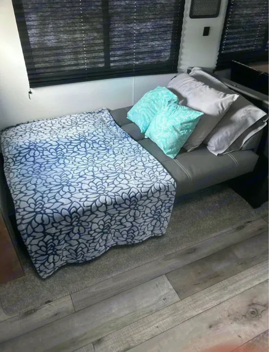 Cozy RV rental living space with a comfy futon, soft floral blanket, and light blue pillows. Ready for relaxation.. Keystone RV Springdale 2022