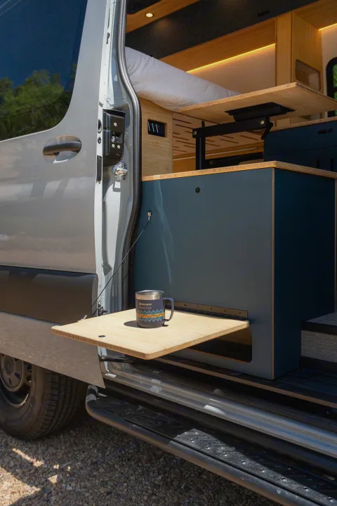 Custom camper van interior for RV rental adventures. Features a cozy bed, pull-out table & clever storage.. Geotrek Flatiron Summit 2025