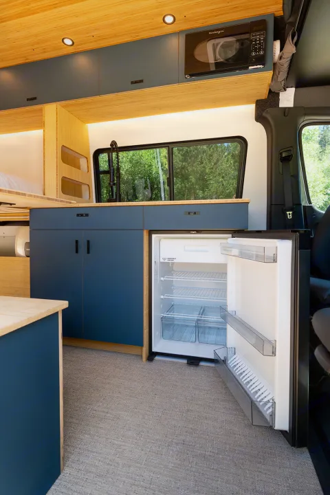 Modern RV rental kitchen with open fridge, microwave, bamboo walls, and blue cabinetry.. Geotrek Flatiron Summit 2025