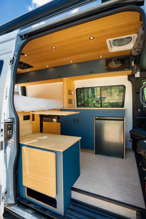 Modern rv rental camper van interior: compact kitchen, fold-out dining, comfortable bed, bamboo and blue accents.. Geotrek Flatiron Summit 2025