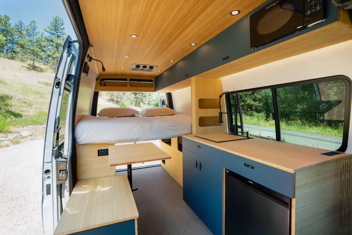 Modern RV rental interior featuring a cozy bed, full kitchen, and flexible dining table for comfortable road trips.. Geotrek Flatiron Summit 2025