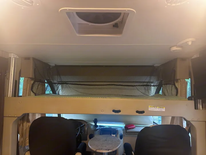 Explore this RV rental's interior: a comfortable cab-over bunk with safety netting above the driver's cockpit.. Thor Axis 2018