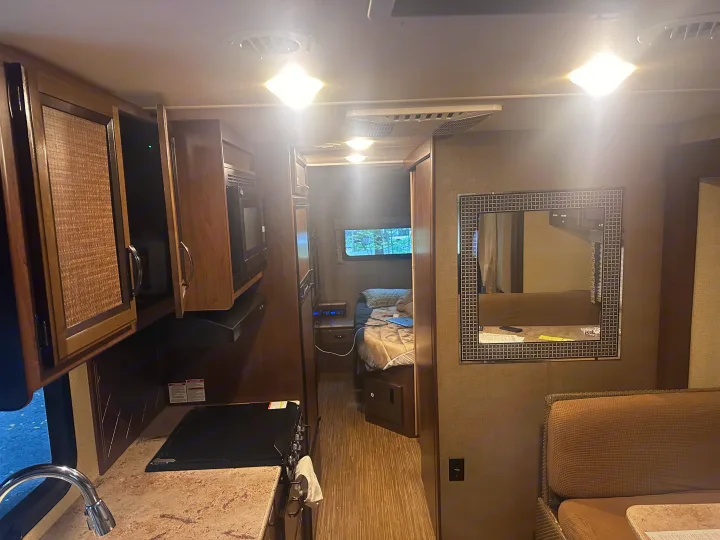 Well-equipped RV rental interior with kitchen, cozy bedroom, and seating area for comfortable travel.. Thor Axis 2018
