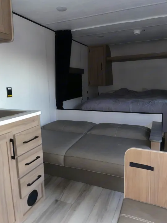 Inside this RV rental: compact living with a bed, sofa, and mini-kitchen. Ideal for comfortable travel.. Colman 23B 2025