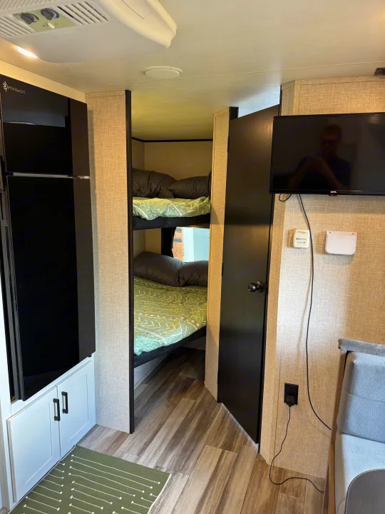 Cozy RV rental interior showcasing bunk beds, a mounted TV, and a tall refrigerator, ideal for family travel.. Jayco Jay Flight 197MB 2025