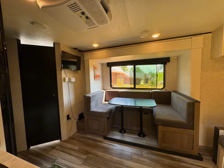 Spacious RV rental interior featuring a cozy U-shaped dinette with a table, wall-mounted TV, and large window.. Jayco Jay Flight 197MB 2025