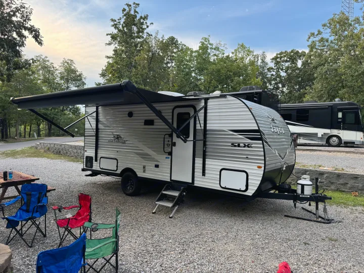 An inviting Jayco RV rental with its awning extended, surrounded by camping chairs and a picnic table at a gravel site.. Jayco Jay Flight 197MB 2025