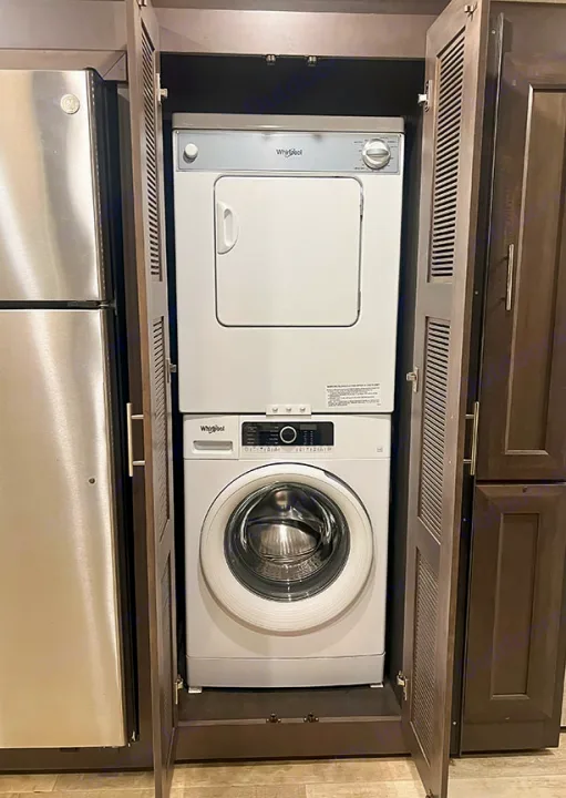 Stacked white Whirlpool washer and dryer within dark cabinetry in this RV rental for convenient laundry.. Thor Motor Coach 2023