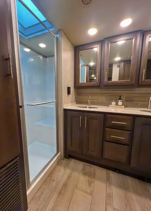 Modern RV rental bathroom: glass shower with skylight & vanity featuring ample cabinet storage.. Thor Motor Coach 2023