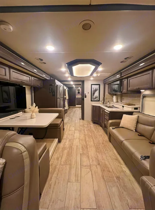 This RV rental shows a modern, spacious interior with a living room, kitchen, and dining area down a long hallway.. Thor Motor Coach 2023