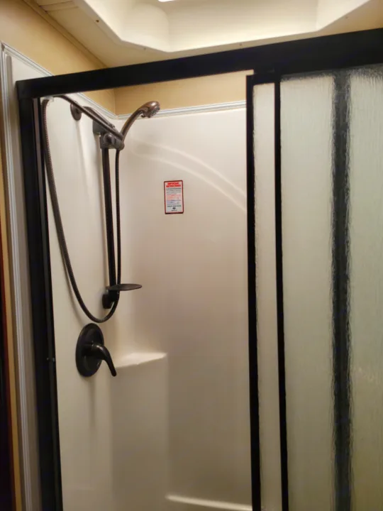 Compact RV rental shower with molded white interior, black fixtures & frosted glass doors.. Forest River Berkshire 390-Bunkhouse 2012