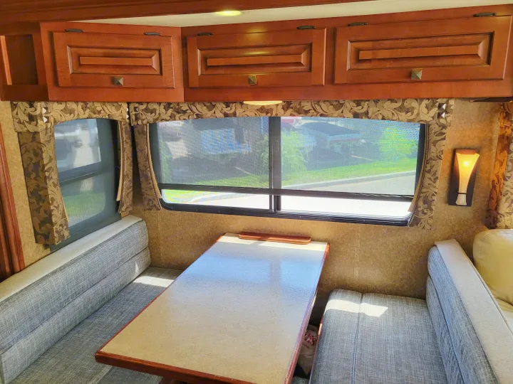 RV rental interior featuring a cozy dinette with wooden cabinets and bright windows offering an outside view.. Forest River Berkshire 390-Bunkhouse 2012