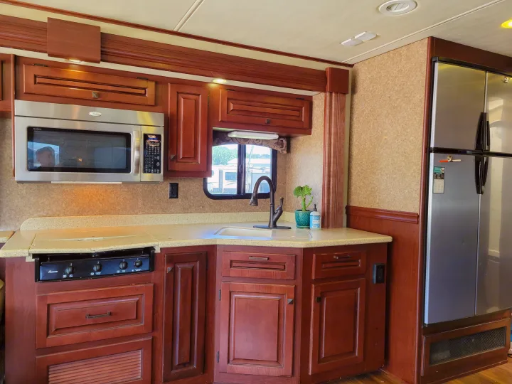 Spacious RV rental kitchen featuring wood cabinets, light counters, stainless steel microwave, stove, sink, and fridge.. Forest River Berkshire 390-Bunkhouse 2012
