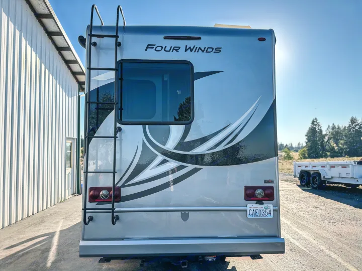 Back of a silver Four Winds RV rental with a ladder, graphic details, and Washington plate CAE0354. Parked outdoors.. Thor Four Winds 2019