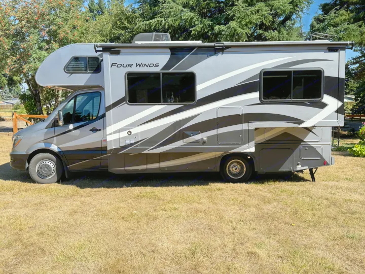 A modern "Four Winds" RV rental in grey and black, shown parked on a sunlit lawn. Ready for your next journey.. Thor Four Winds 2019