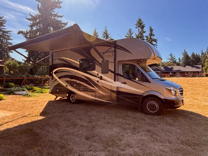 This RV rental, a sleek motorhome with an extended awning, sits on a sunny lawn, ready for your next outdoor adventure.. Thor Four Winds 2019
