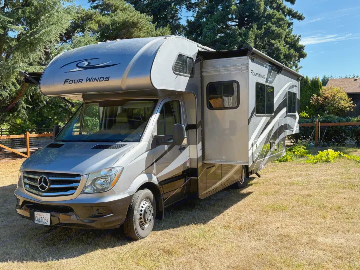 Grey Four Winds RV rental (Mercedes-Benz Sprinter) with slide-out extended, parked on a sunny, grassy field.. Thor Four Winds 2019