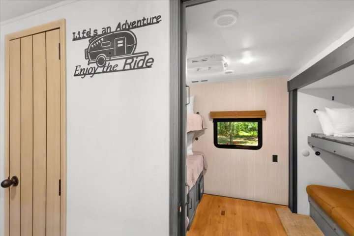 Interior of an RV rental: bunk beds, a window overlooking trees, and "Life's an Adventure, Enjoy the Ride" wall art.. Forest River Puma 2026