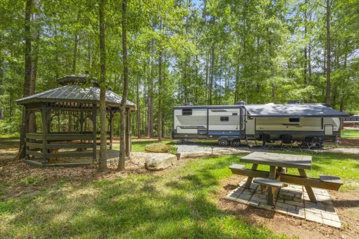 Serene RV rental campsite with a spacious RV, gazebo, and picnic table amidst lush trees for outdoor relaxation.. Forest River Puma 2026