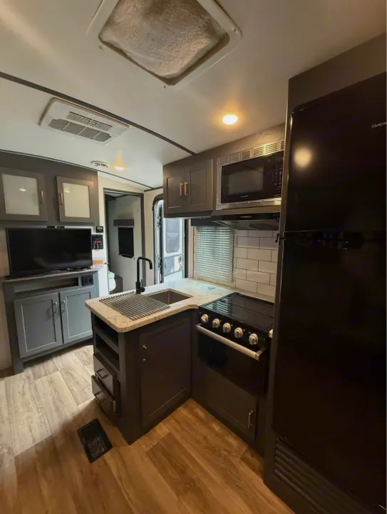 Modern RV rental interior featuring a well-equipped kitchen with sink, stove, microwave, fridge, & TV setup.. Keystone RV Bullet Ultra Lite 2022