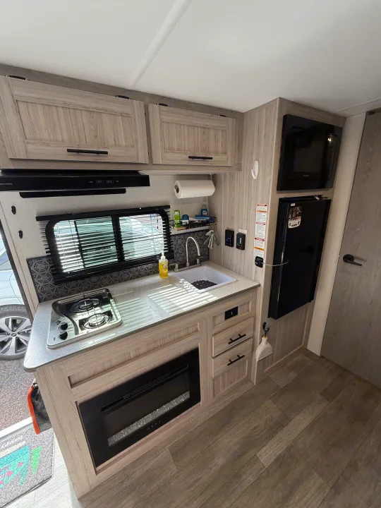 Explore this modern RV rental kitchen featuring a sink, stovetop, microwave, fridge, and an electric fireplace.. Heartland RVs Pioneer 2025