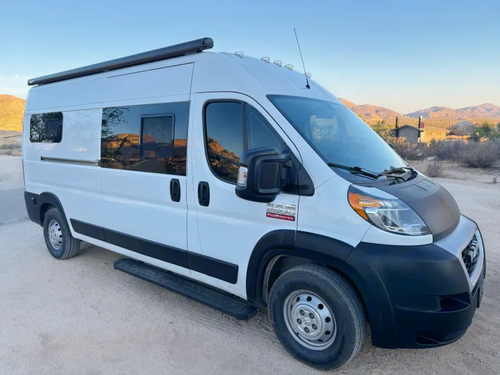 White Ram ProMaster camper van RV rental in a desert setting with mountains in the background, parked on a dirt road.. RAM Promaster 2500 2020