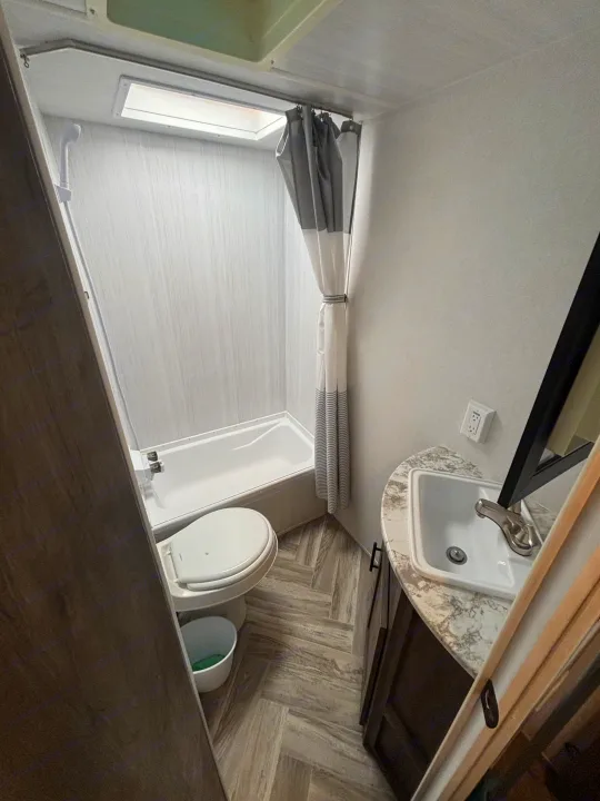 Compact RV rental bathroom with tub/shower, toilet, & sink. Perfect for travel!. Forest River Wildwood X-Lite 2023