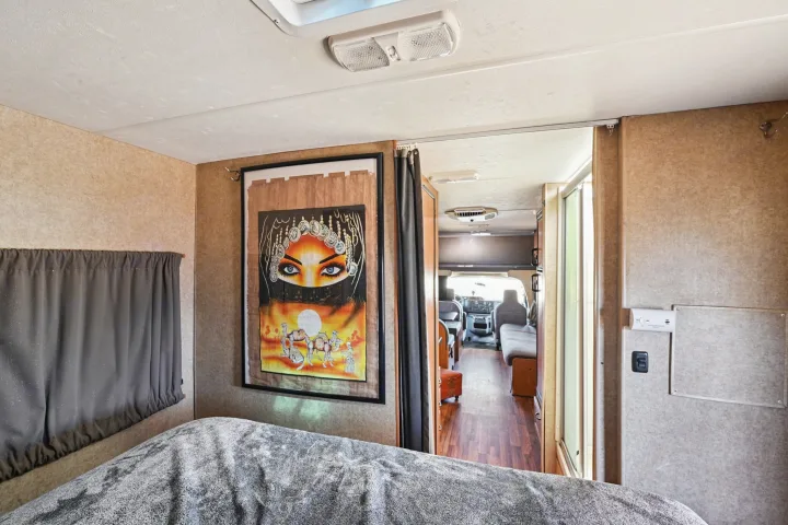 RV rental interior: foreground bed with a blanket, framed artwork on the wall, and an open hallway towards the front.. Thor Majestic 2012