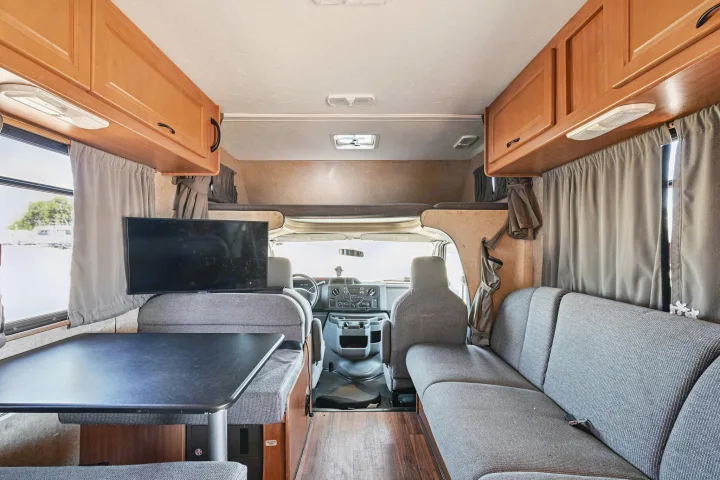 View of an rv rental's living space, featuring a dinette, sofa, TV, and cab-over bunk bed for travelers.. Thor Majestic 2012