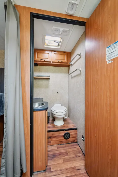 Compact RV rental bathroom features: toilet, small sink, storage cabinets, and skylight, ready for your trip.. Thor Majestic 2012
