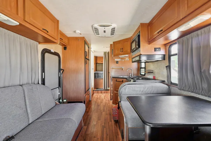 Spacious rv rental interior featuring a full kitchen, dining booth, and sofa. Light wood cabinetry and grey upholstery throughout.. Thor Majestic 2012