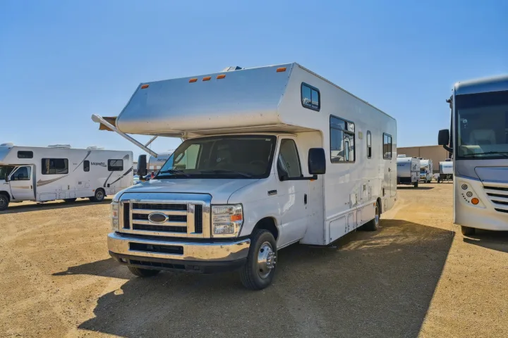 White Class C RV for rent on a sunny gravel lot, surrounded by other motorhomes, ready for adventure.. Thor Majestic 2012