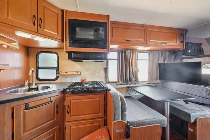 Inside an rv rental: functional kitchen with microwave, stove, sink, and dining area with TV. Compact and ready for adventure.. Thor Majestic 2012