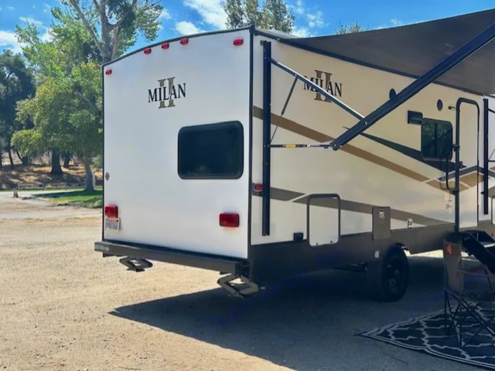 Milan travel trailer RV rental, white with brown accents, parked at a sunny campsite with its awning extended.. Eclipse Recreational Vehicles Milan II 2024