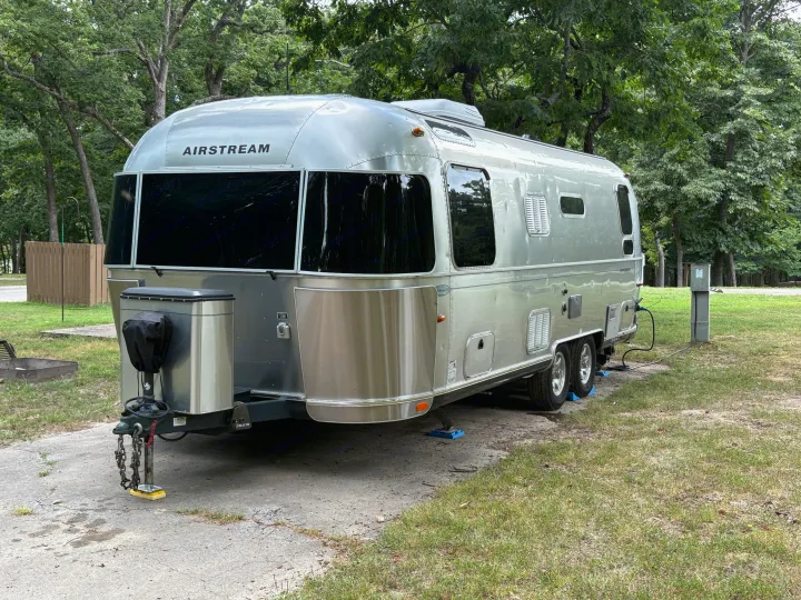 This iconic Airstream RV rental is parked and set up at a serene, tree-lined campsite.. Airstream Flying Cloud 2012
