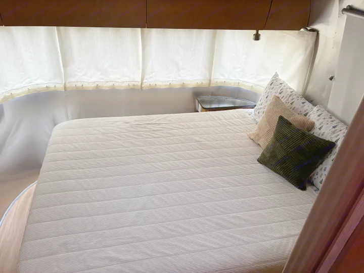 Cozy RV rental bedroom with striped bed, throw pillows, and curved walls.. Airstream Flying Cloud 2012