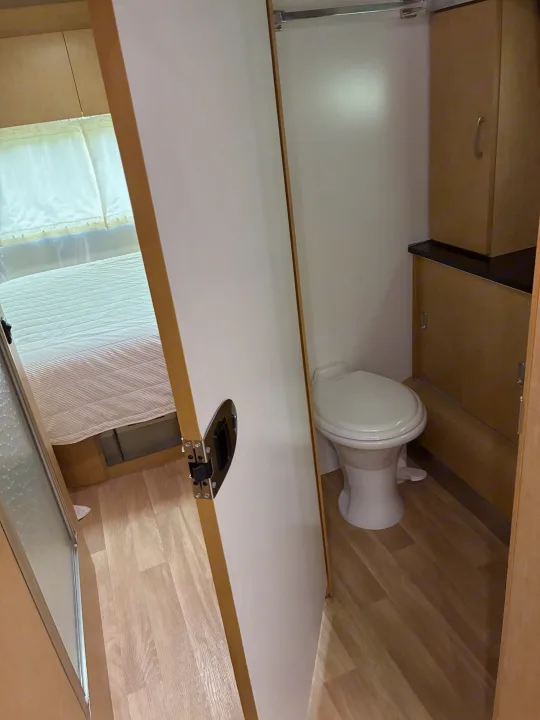 View inside an RV rental showing a compact bedroom and a functional bathroom with a toilet and storage cabinets.. Airstream Flying Cloud 2012