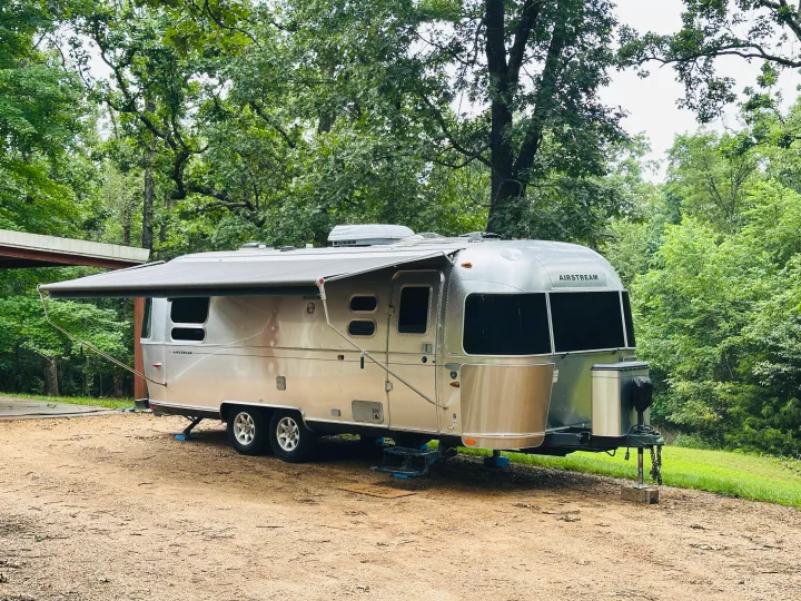 Enjoy nature with this Airstream RV rental, parked among trees with its awning extended for shade.. Airstream Flying Cloud 2012