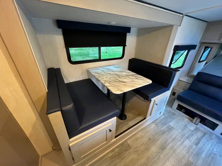 Modern RV rental interior showing a light-toned dinette, dark cushioned benches, and scenic window.. Coachmen Apex 2026