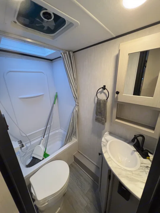 Inside an RV rental: a compact bathroom with a shower/tub, toilet, and sink. Practical design for your travels.. Coachmen Apex 2026