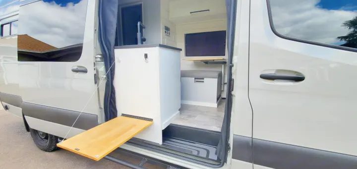 Explore this RV rental's versatile design: an open side door reveals a compact kitchen, seating, and an exterior pull-out table.. Activan Cypress 170 2022