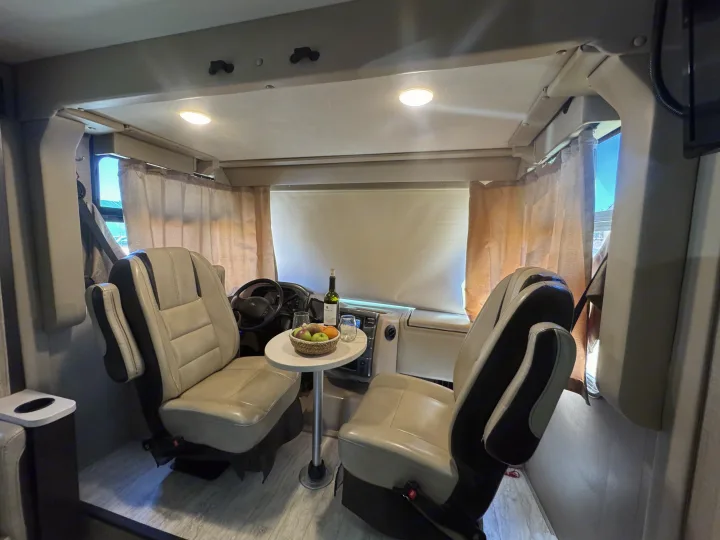 Cozy RV rental interior: cockpit seats swivel to create a lounge with a table, wine, and fruit. Perfect for travel!. Thor Axis 2020