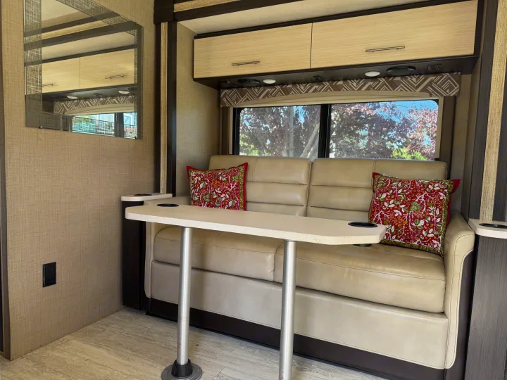 RV rental interior showing a comfortable sofa with patterned pillows, a table with cup holders, and overhead cabinets.. Thor Axis 2020