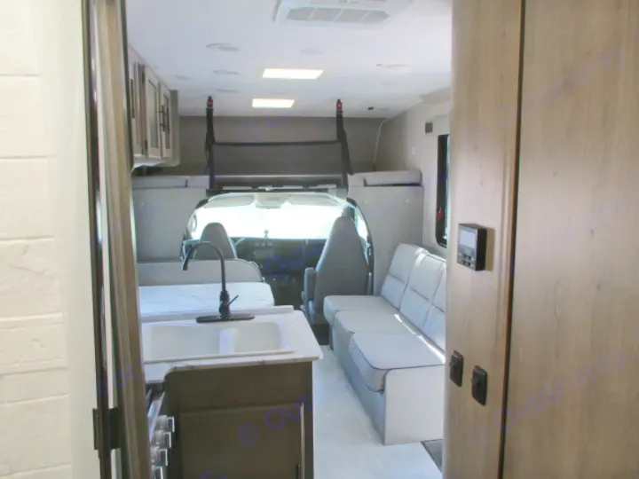 Clean rv rental interior showing a kitchen with sink, comfy sofa, and an overhead sleeping area above the cab.. Coachmen Freelander 27QB 2021