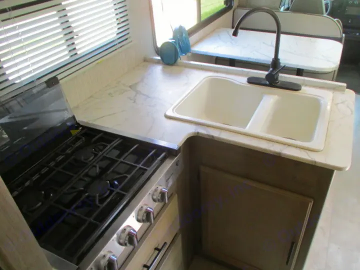 Clean RV rental kitchen area showing a gas stove, double sink, black faucet, and white marble-look counters.. Coachmen Freelander 27QB 2021