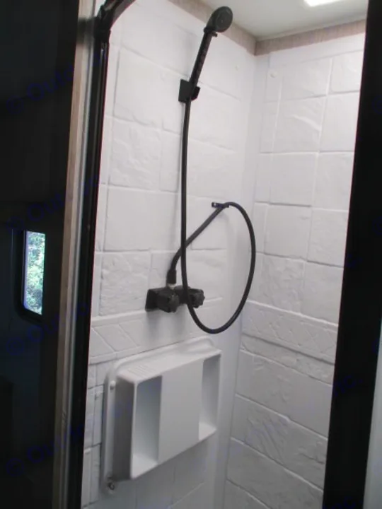 Compact RV rental shower: white textured walls, black handheld shower, and integrated caddy for toiletries.. Coachmen Freelander 27QB 2021