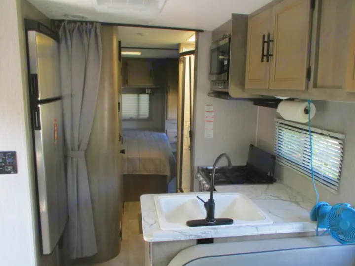 RV rental interior: A compact kitchen with a sink, stove, and microwave, next to a fridge and a cozy bedroom.. Coachmen Freelander 27QB 2021
