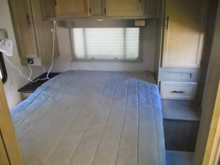 Inside an RV rental: a light-colored bedroom with a large bed, window, overhead cabinets, and built-in storage.. Coachmen Freelander 27QB 2021