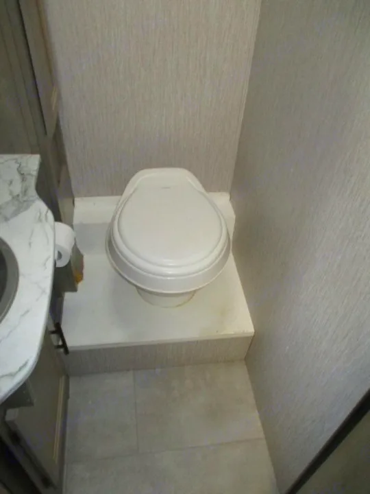RV rental's compact bathroom: white toilet on a raised platform, next to a marble-patterned sink. Gray textured walls.. Coachmen Freelander 27QB 2021